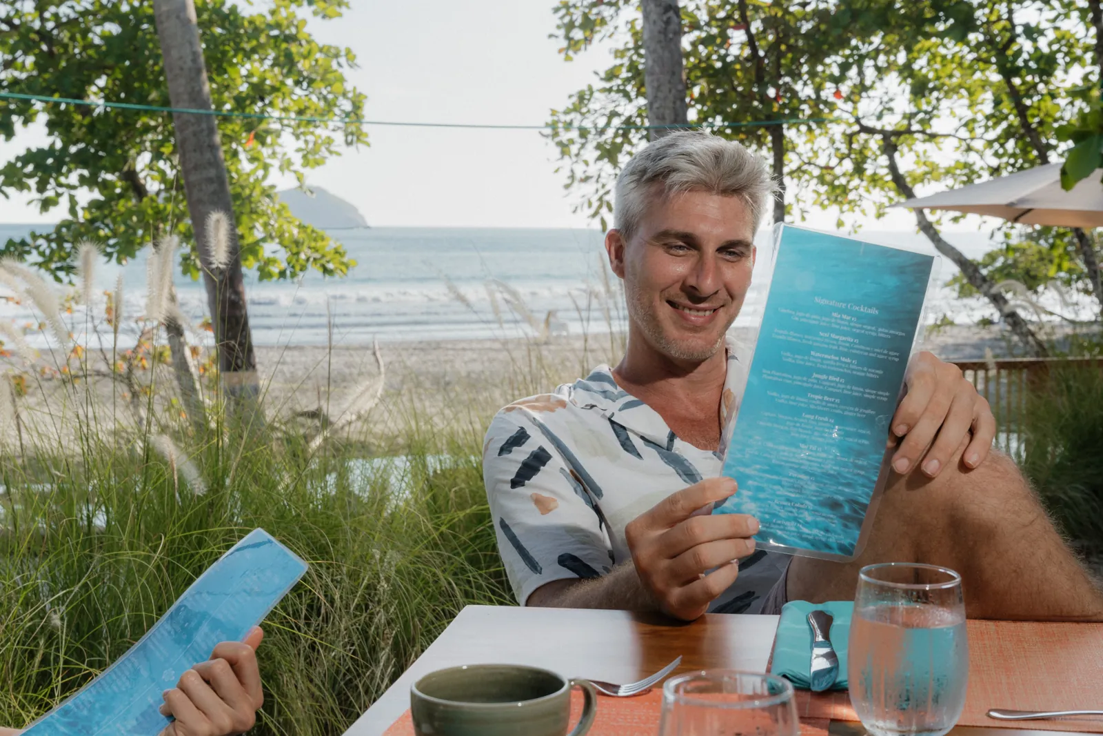 A guest reading the cocktail menu at a table facing the ocean
